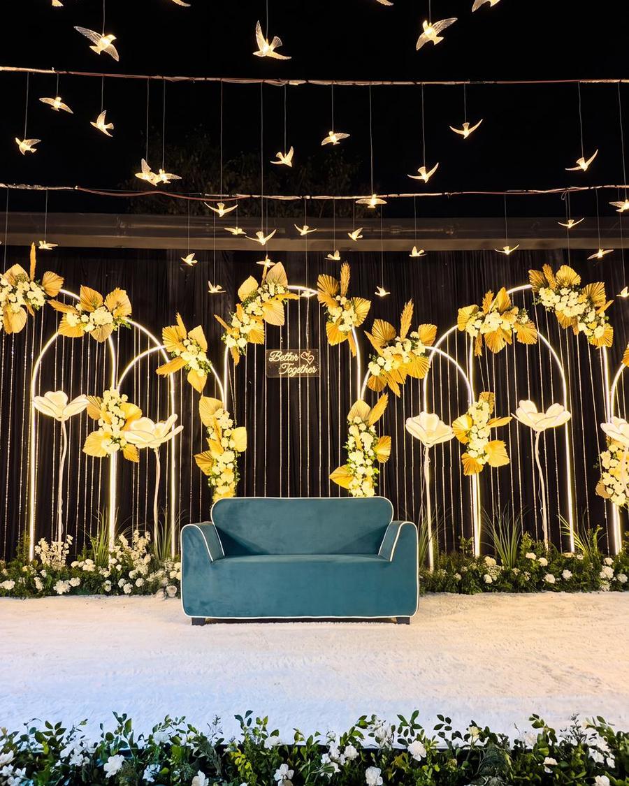 An engagement stage with gold arches, white flowers and lit paper birds overhead