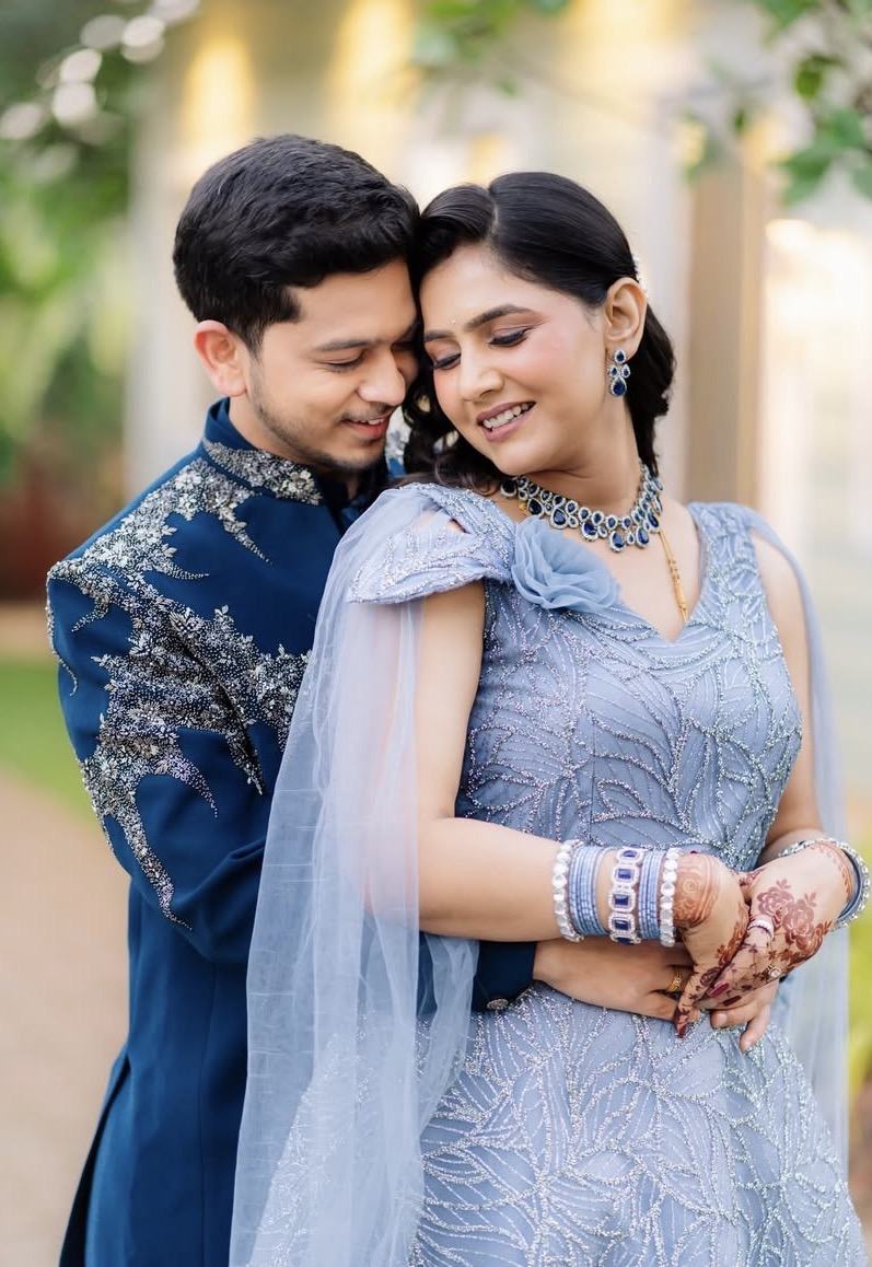 A couple in matching blue, his arms around her, at golden hour