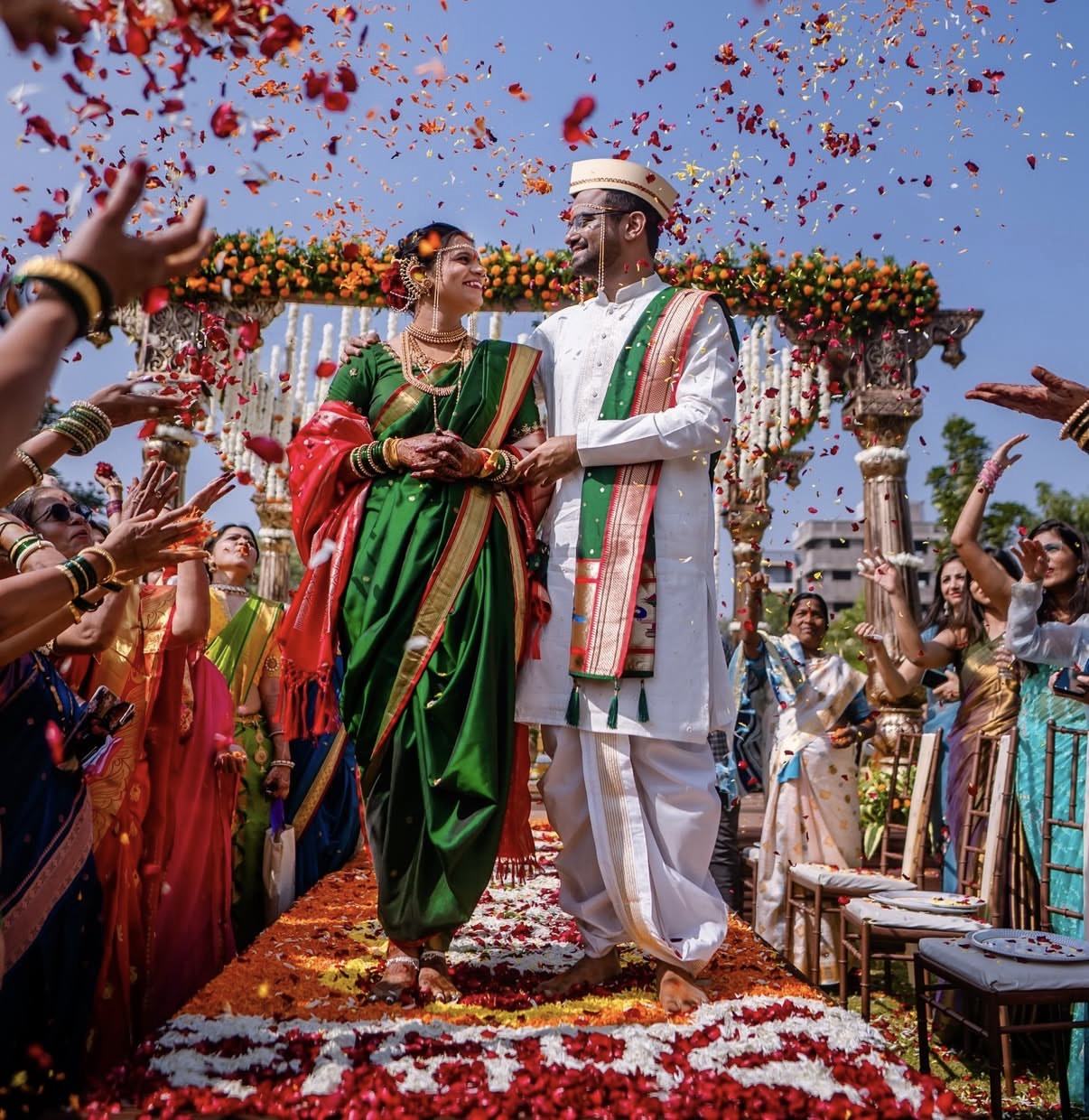 A couple in green and white walking out under a shower of rose petals
