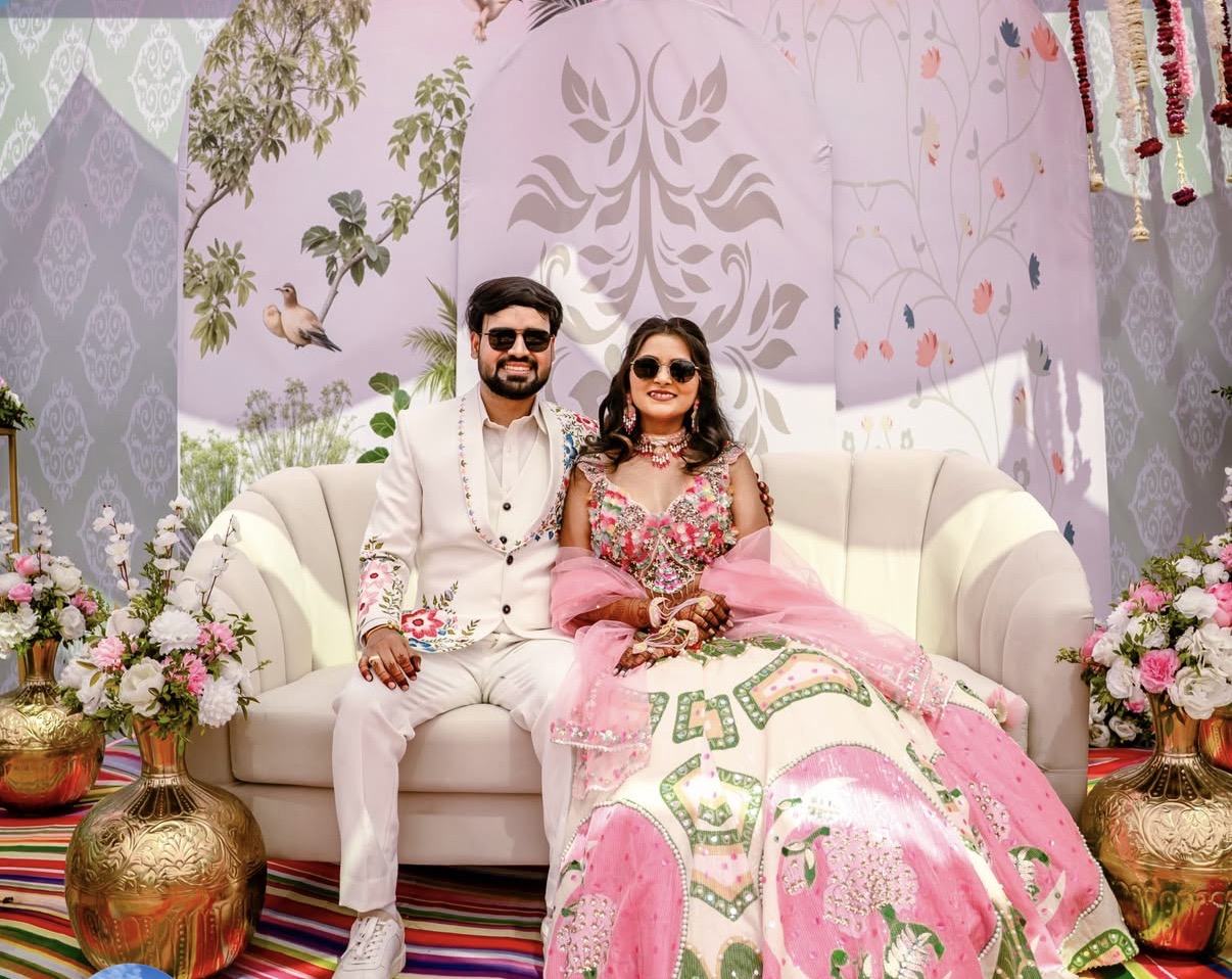 A couple in white and pink on a curved sofa against a pastel painted backdrop
