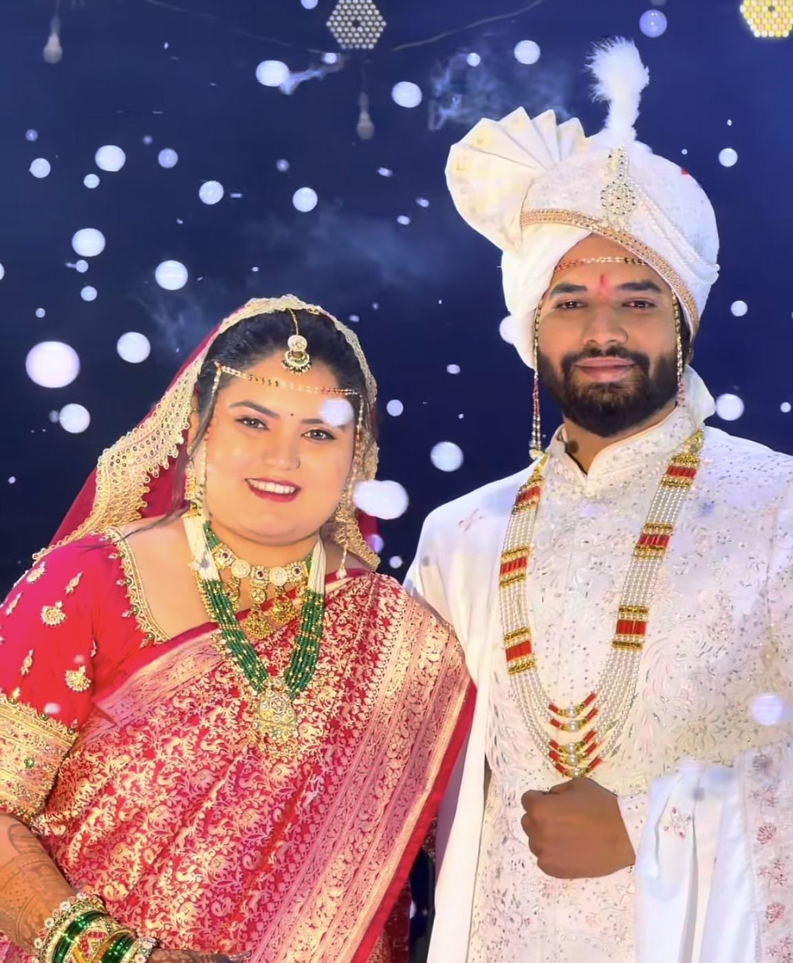 A bride in red Banarasi and a groom in white sherwani under a night of lights