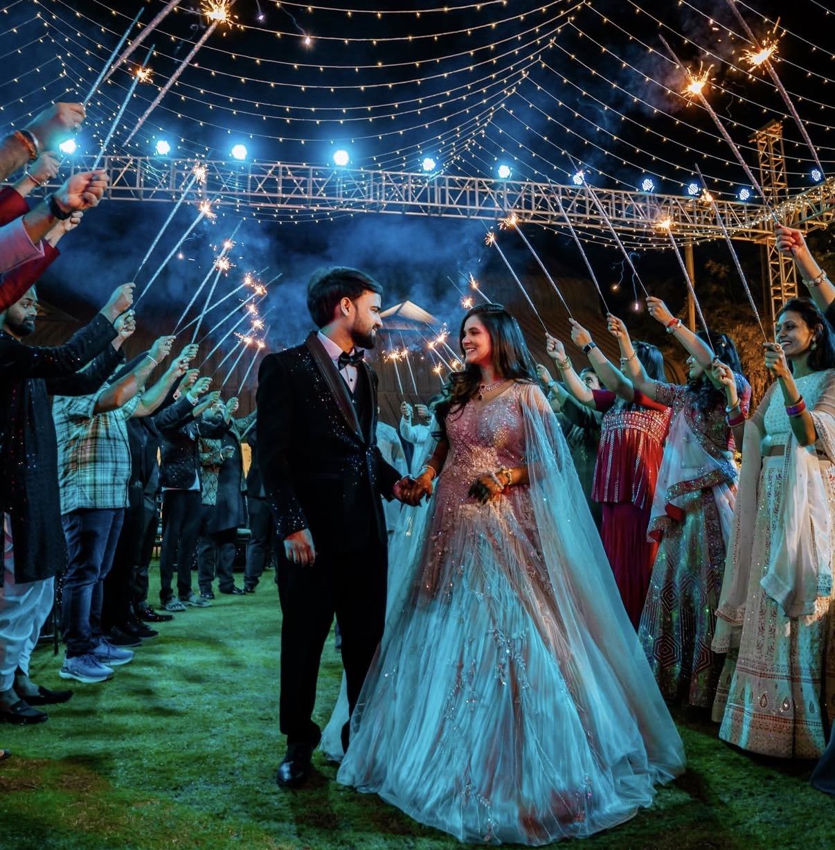 A couple walking through a tunnel of sparklers held by their guests at night