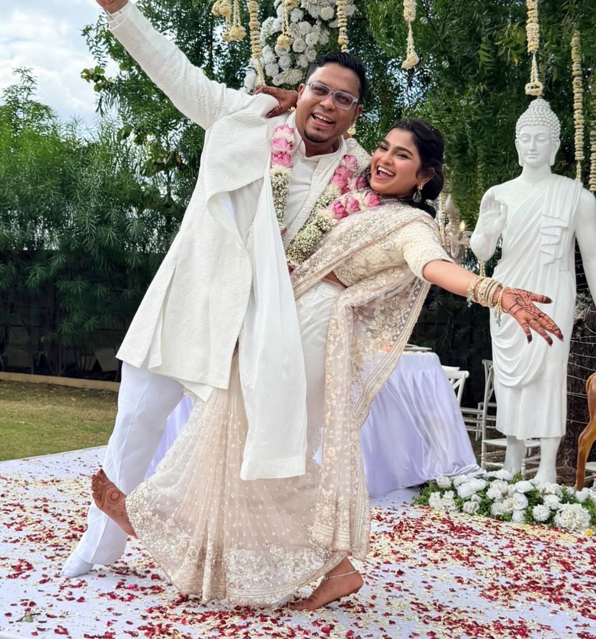 A couple in white and pink garlands, mid-dance on a petal-strewn floor