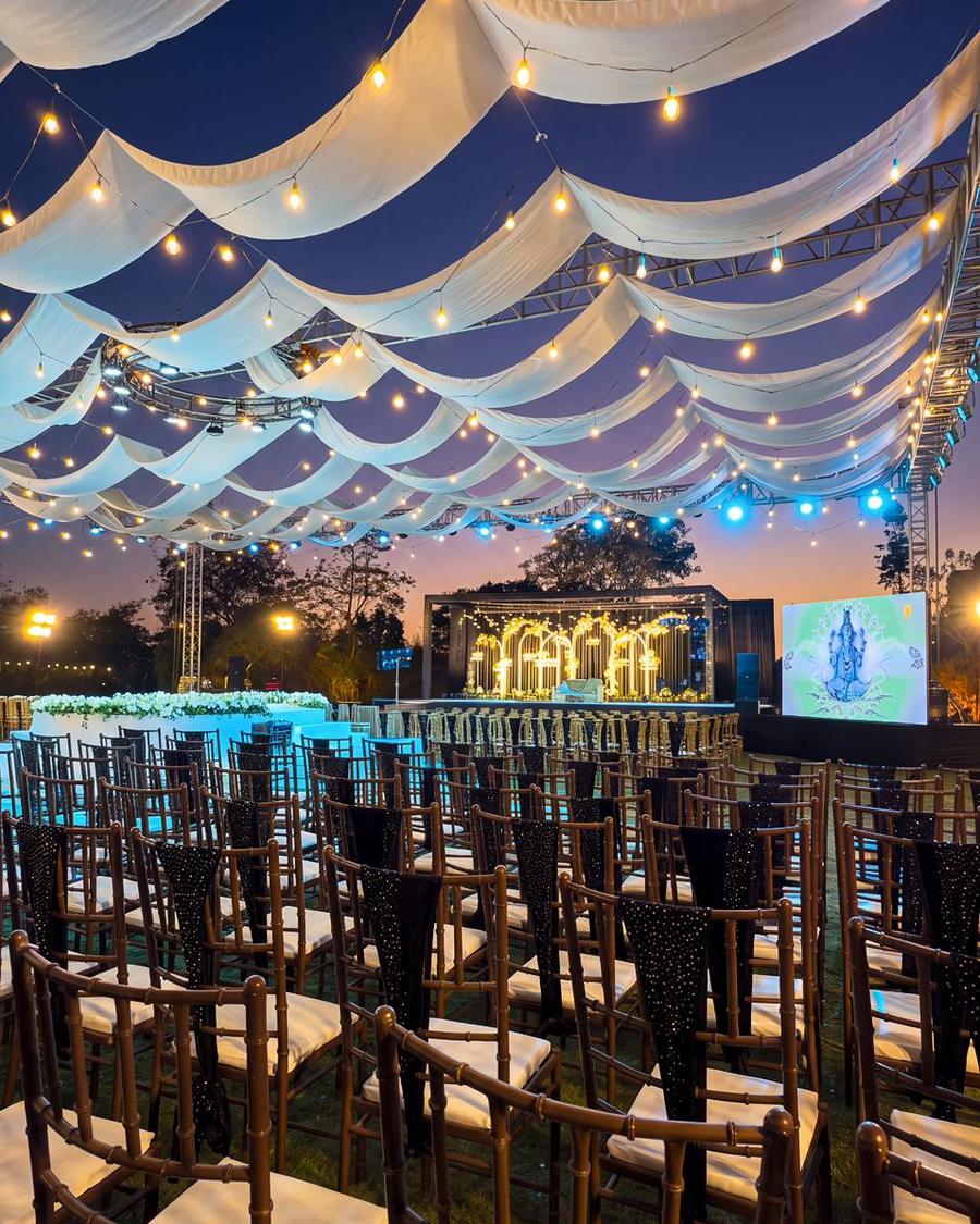 A full canopy of draped fabric and bulbs over the lawn, with the stage lit beyond