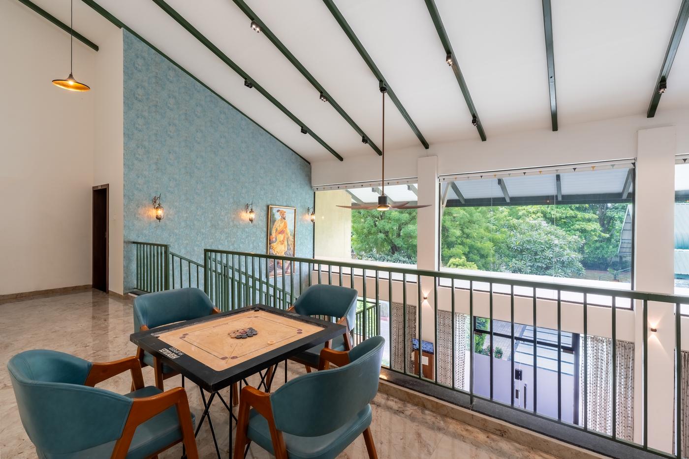 A carrom board and four chairs on the mezzanine, trees through the glass