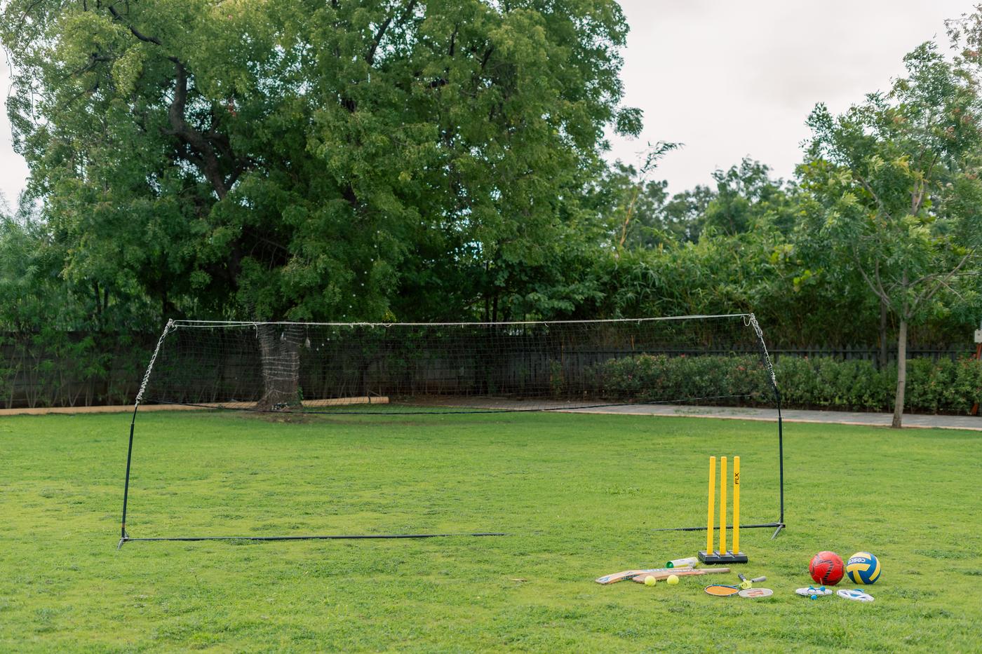 A lawn set up with a badminton net, cricket stumps, bats and balls