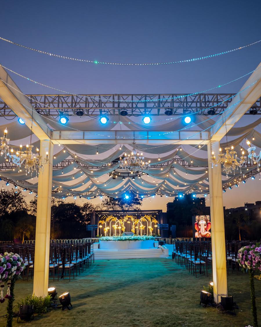 A lit walkway of chandeliers and draped fabric leading to the stage at dusk