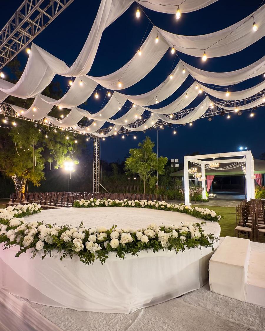A round white stage ringed with white roses under draped fabric and bulbs